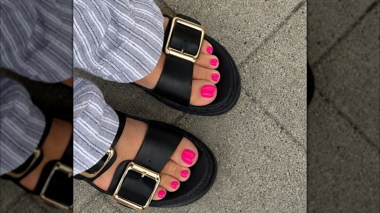 Gros plan des pieds d'une femme, portant du vernis à ongles rose vif et de grosses sandales noires
