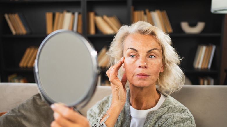 Une femme plus âgée se regardant dans le miroir et touchant son visage d'une main