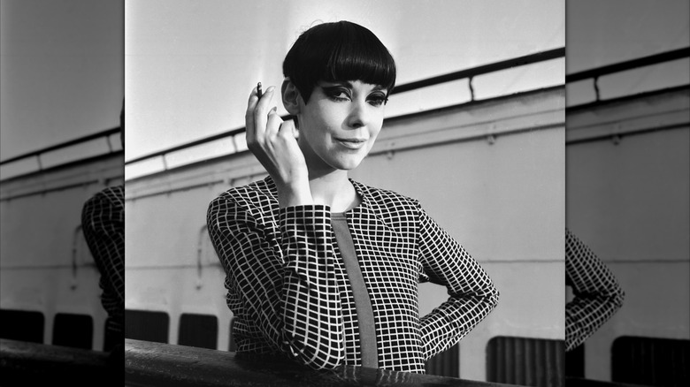Un portrait de Peggy Moffitt tenant une cigarette et souriant en noir et blanc