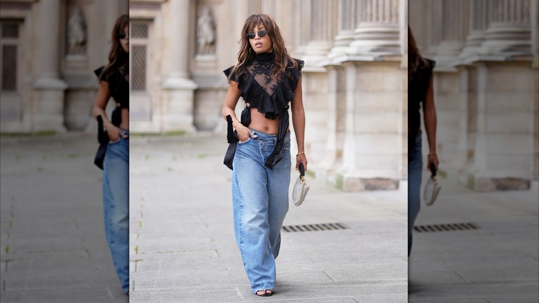 Une femme portant un jean bleu et un crop top à volants avec un col haut.