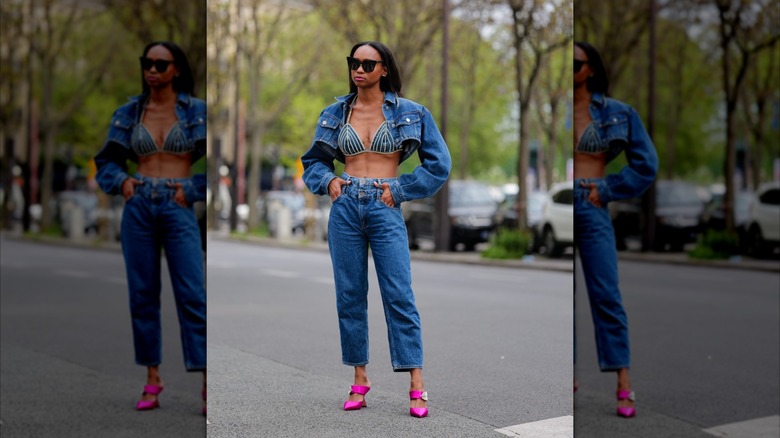 Une femme porte un jean bleu, un soutien-gorge en jean et une veste courte en jean.