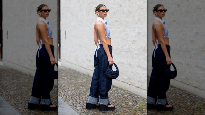 Une femme à la Fashion Week de Berlin 2025 porte un crop top bleu clair avec un dos exposé et un jean ample.