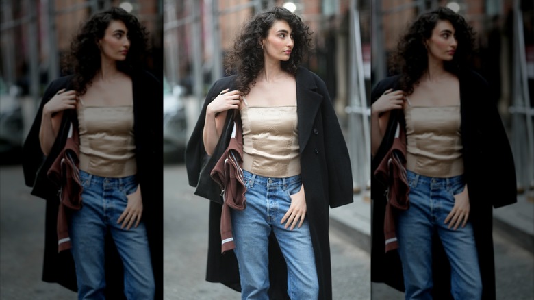 Une femme porte une camisole en satin beige, un jean bleu et un manteau en laine noire.