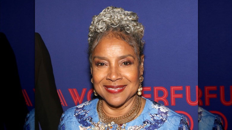 Phylicia Rashad sourit avec une coiffure en chignon et des boucles d'oreilles en perles