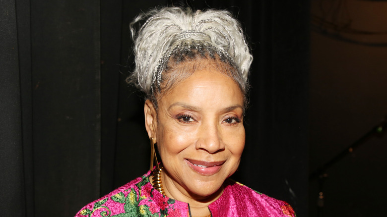 Phylicia Rashad sourit avec ses cheveux gris en chignon et une veste rose vif