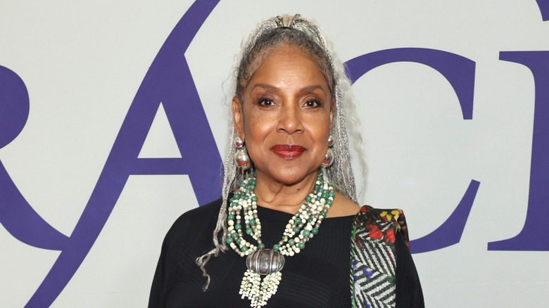 Phylicia Rashad sourit avec des tresses argentées portant un collier de perles tendance