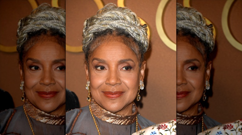 Phylicia Rashad sourit avec des bijoux en or et ses cheveux en chignon tressé