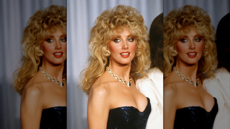 Morgan Fairchild posant dans une robe bleue scintillante avec un collier en chaîne dorée.