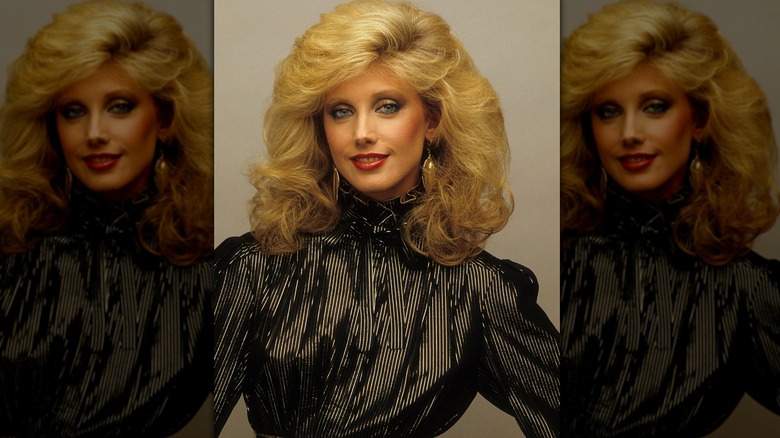 Morgan Fairchild posant dans un haut noir avec des boucles d'oreilles dorées.