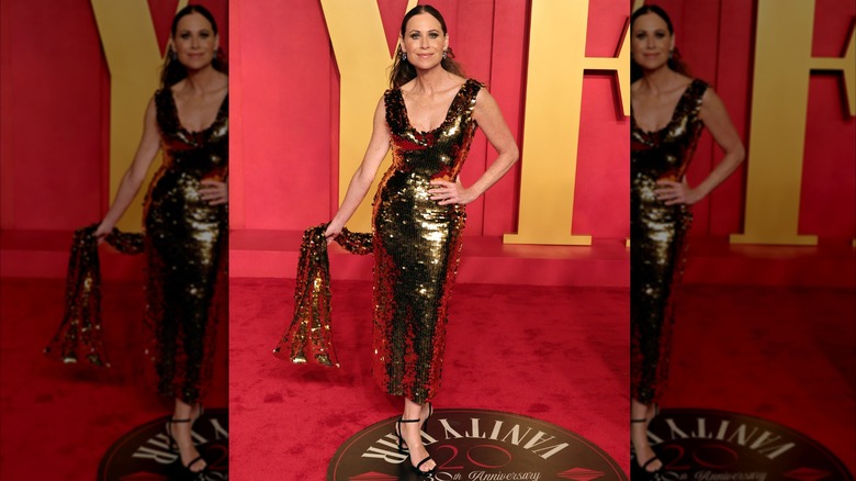 Minnie Driver posant lors d'une soirée des Oscars vêtue d'une robe dorée scintillante.