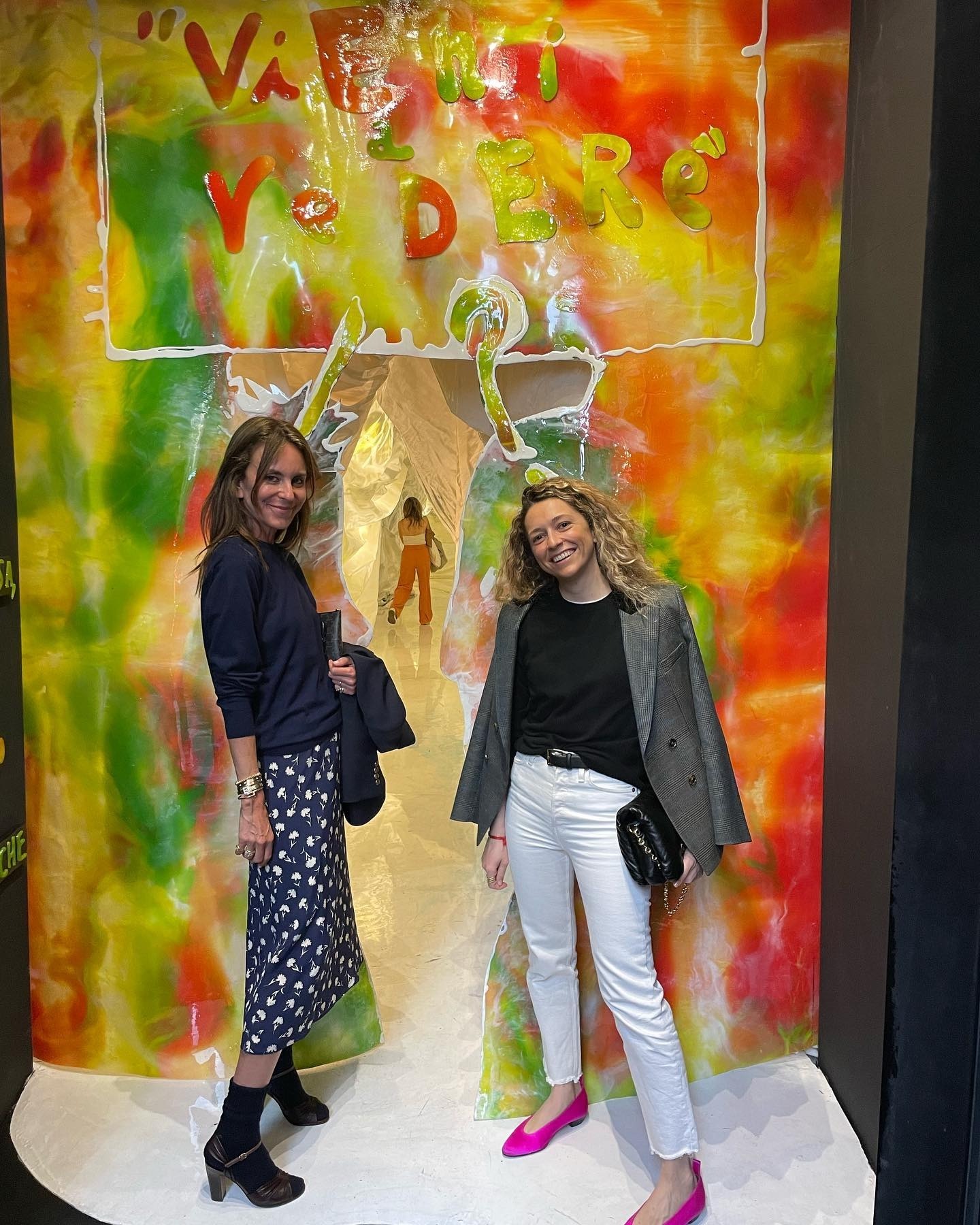 Alison en look pull avec une jupe midi imprimée et des bottines lors d'une exposition d'art avec une amie.