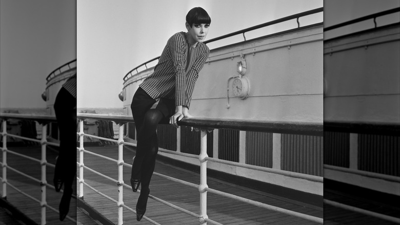 Peggy Moffitt posant sur la rambarde d'un navire vêtue d'une veste à carreaux avec une jupe et des collants noirs.
