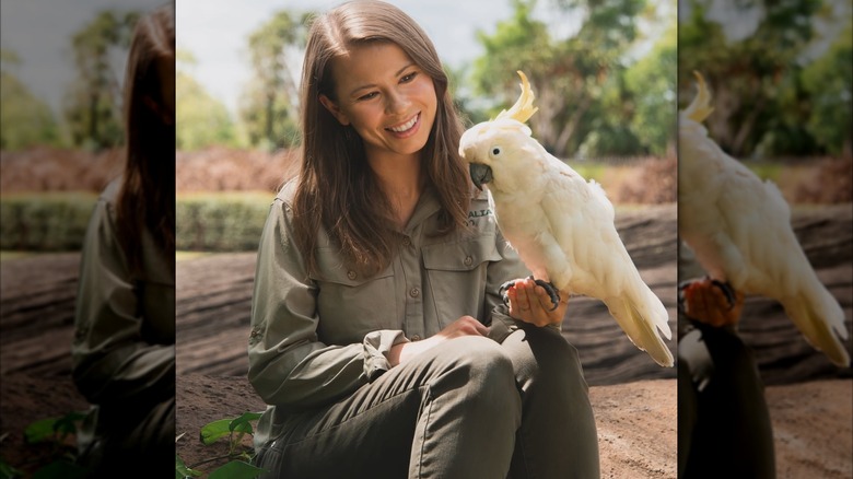 Bindi Irwin tout en kaki, tenant un oiseau au zoo d'Australie.