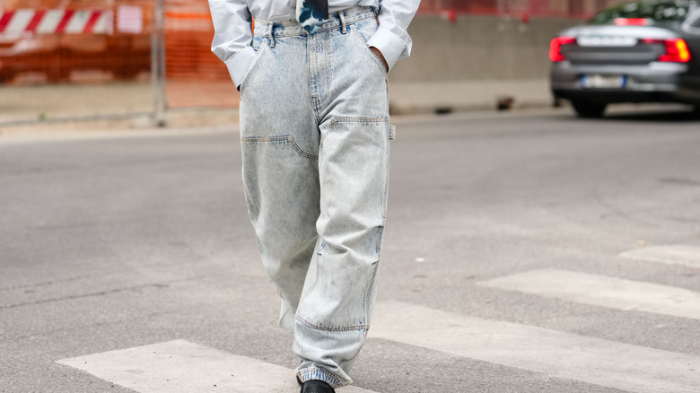 Gros plan sur les jambes d'une personne qui marche, portant un jean délavé à l'acide et une chemise blanche