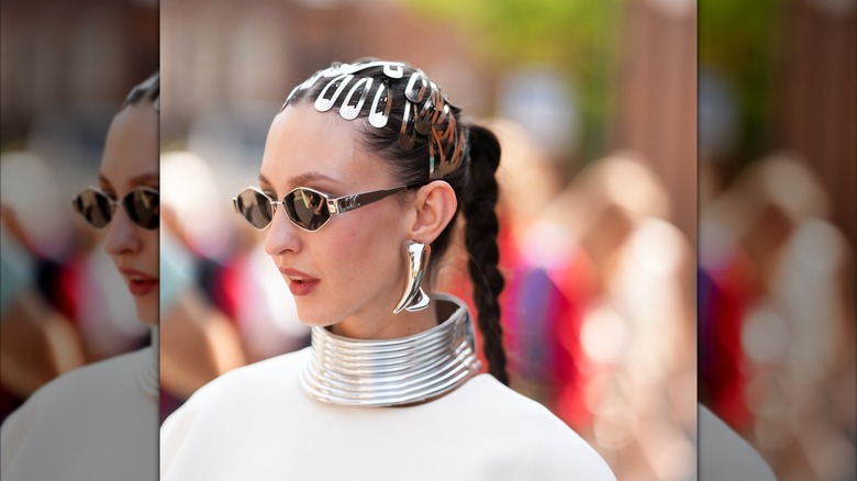 Une femme portant des boucles d'oreilles chromées surdimensionnées, un tour de cou et plusieurs barrettes.