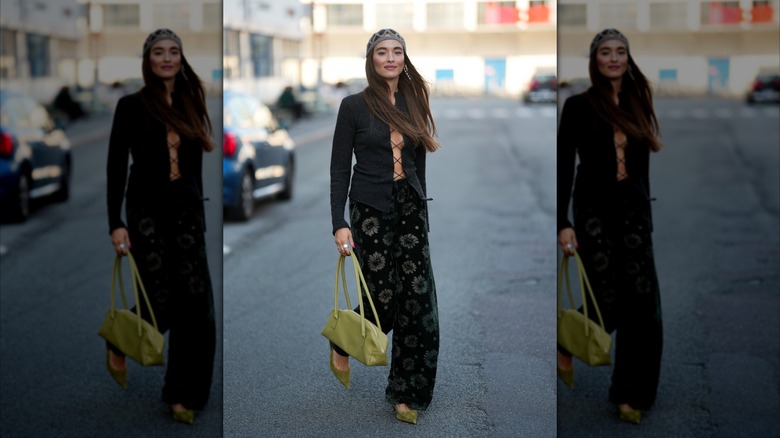Une femme portant un pantalon en velours fleuri, des talons en velours vert et un chemisier à lacets noir.