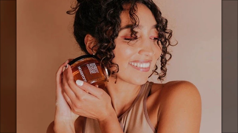 Aliyah Marandiz, fondatrice de Sugardoh, posant avec un pot de pâte à épiler près de son visage.