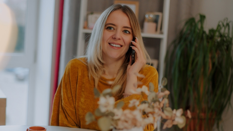 Une femme portant un pull jaune moutarde tout en parlant au téléphone
