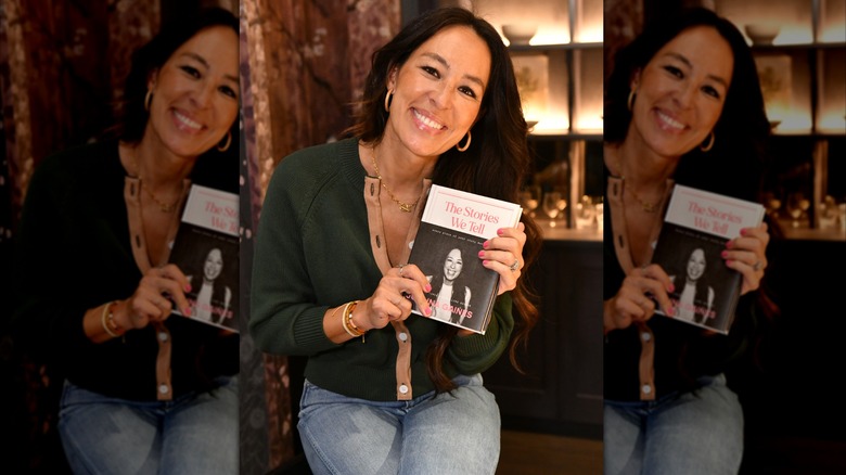 Joanna Gaines posant avec son livre portant un jean et un pull vert foncé.