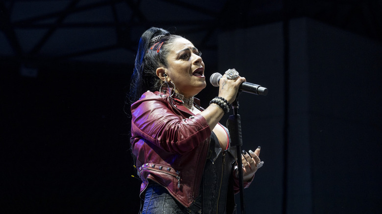 Lisa Velez se produit sur scène vêtue d'une veste en cuir rouge avec une queue de cheval haute.