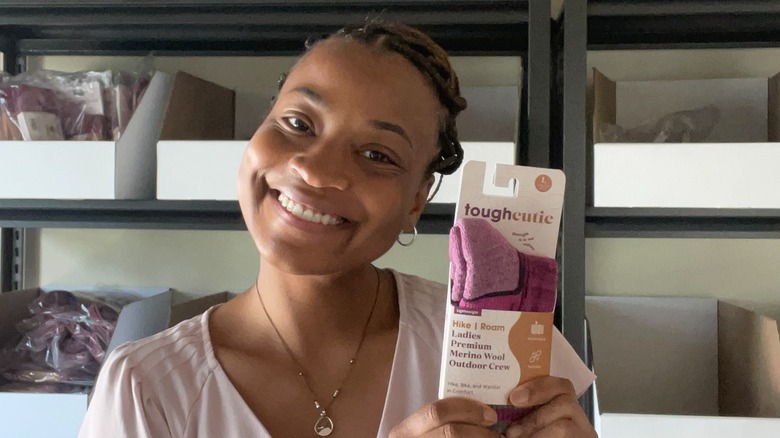 La fondatrice de ToughCutie, Brittany Coleman, porte ses cheveux relevés avec un t-shirt rose clair et de petites créoles tout en exhibant une nouvelle couleur de chaussettes en juillet 2025.