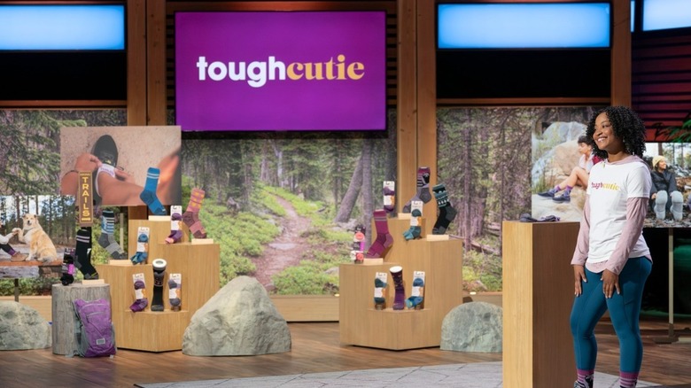 La fondatrice de ToughCutie, Brittany Coleman, porte un t-shirt blanc avec le logo de son entreprise sur une chemise à capuche rose à manches longues avec un jean et ses chaussettes ToughCutie tout en présentant son entreprise sur Shark Tank, diffusé en janvier 2025.