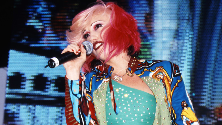Gwen Stefani de No Doubt se produit avec des cheveux roses et blonds, vêtue d'une chemise turquoise et d'une veste colorée.