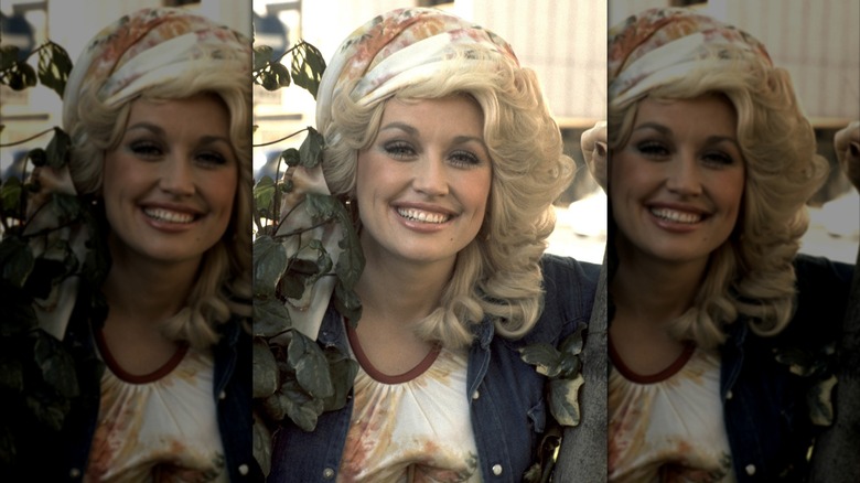 Dolly Parton souriante portant un foulard avec une veste en jean.