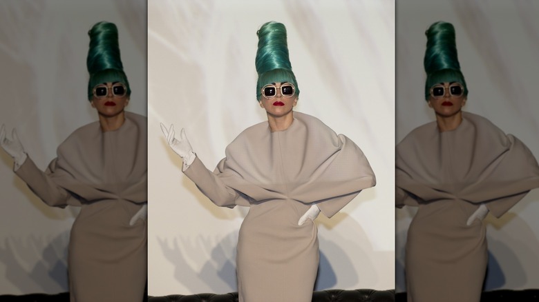 Lady Gaga se produit dans une robe beige avec une coiffure en ruche vert sarcelle et des lunettes de soleil.