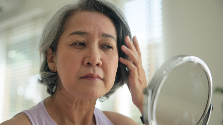 Femme mûre aux cheveux grisonnants se regarde dans un petit miroir rond
