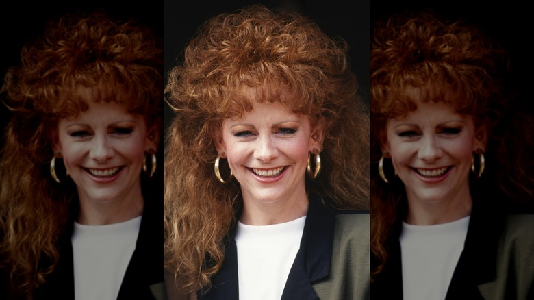 Reba McEntire avec de grands cheveux roux bouclés portant un haut blanc et un blazer en 1990.