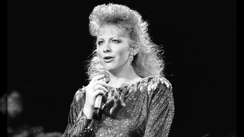 Reba McEntire portant un haut scintillant et des cheveux ébouriffés lors d'une prestation en 1988.