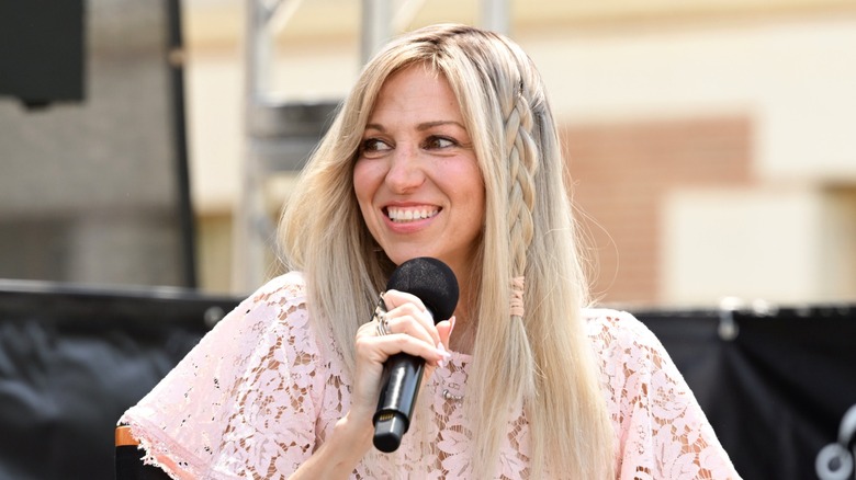 Debbie Gibson portait ses longs cheveux blonds détachés avec une tresse lâche sur le côté et une chemise en dentelle rose pâle lors d'un discours au Los Angeles Times Festival of Books 2026 à Los Angeles.