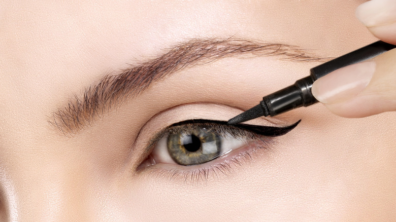 Gros plan d'une personne appliquant une aile d'eye-liner noir avec l'œil ouvert