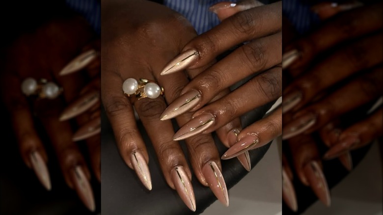 Manucure longue et pointue avec vernis à ongles œil de chat doré et motifs à rayures dorées