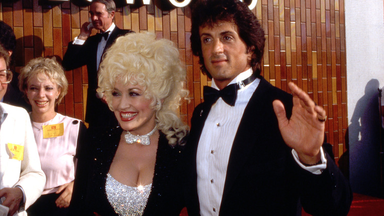 Dolly Parton en 1984 posant avec Sylvester Stallone portant un haut argenté scintillant avec un nœud papillon assorti et une veste noire scintillante.