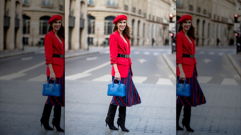 Une femme portant un blazer rouge, une ceinture noire et une jupe rayée bleue et rouge.