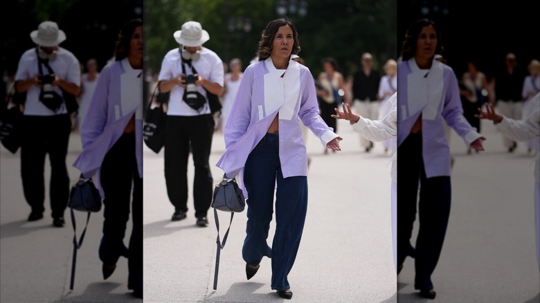 Une femme porte un jean foncé et une chemise boutonnée violet clair et blanche.