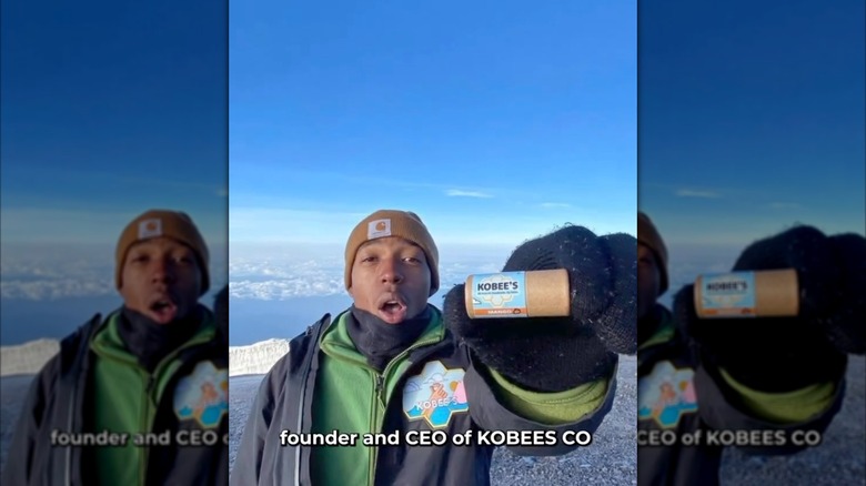 Kobe Harris dans les montagnes enneigées brandissant un baume à lèvres Kobee