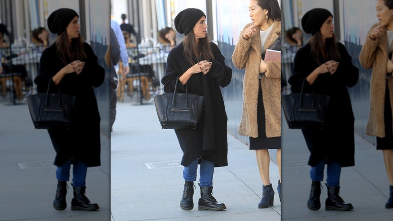 Soleil Moon Frye dans la rue portant un jean, un manteau noir, un bonnet noir et des bottes de combat noires avec un grand sac à main noir.