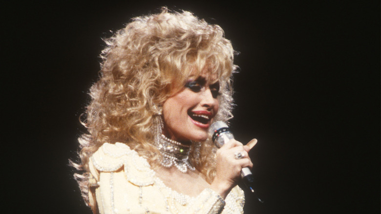 Dolly Parton chante dans un micro avec des cheveux blonds bouclés