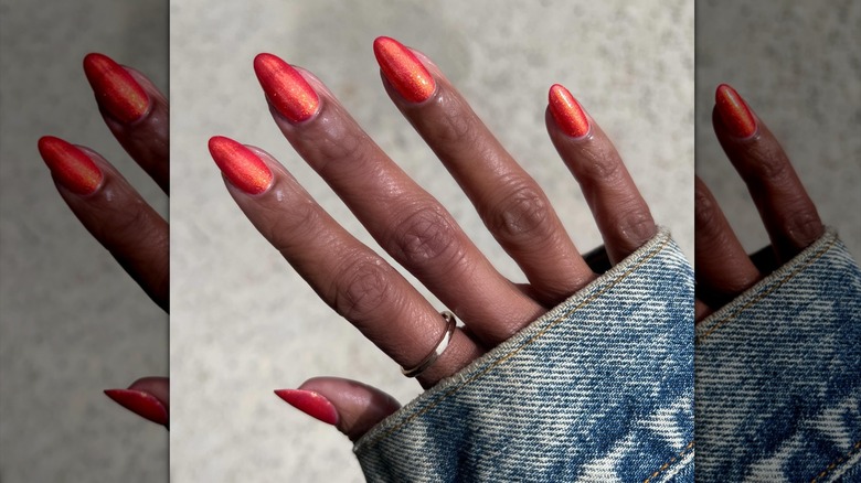 Une main portant du vernis à ongles chatoyant orange brûlé.