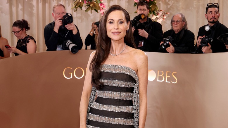 Minnie Driver posant sur le tapis rouge dans une robe à rayures noires et argentées.