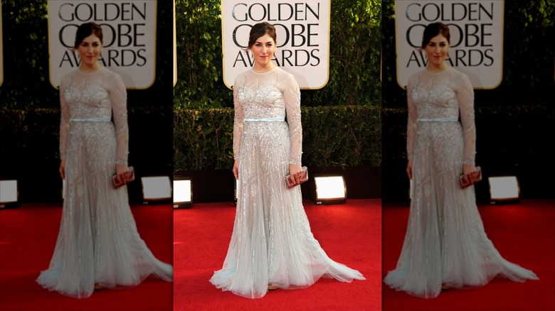 Mayim Bialik sourit dans une robe argentée transparente sur le tapis rouge.