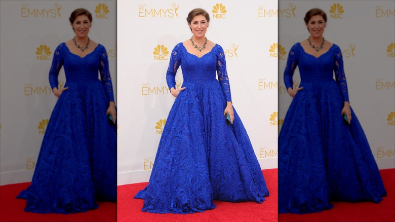 Mayim Bialik pose sur le tapis rouge vêtue d'une robe de bal à manches longues bleu cobalt.