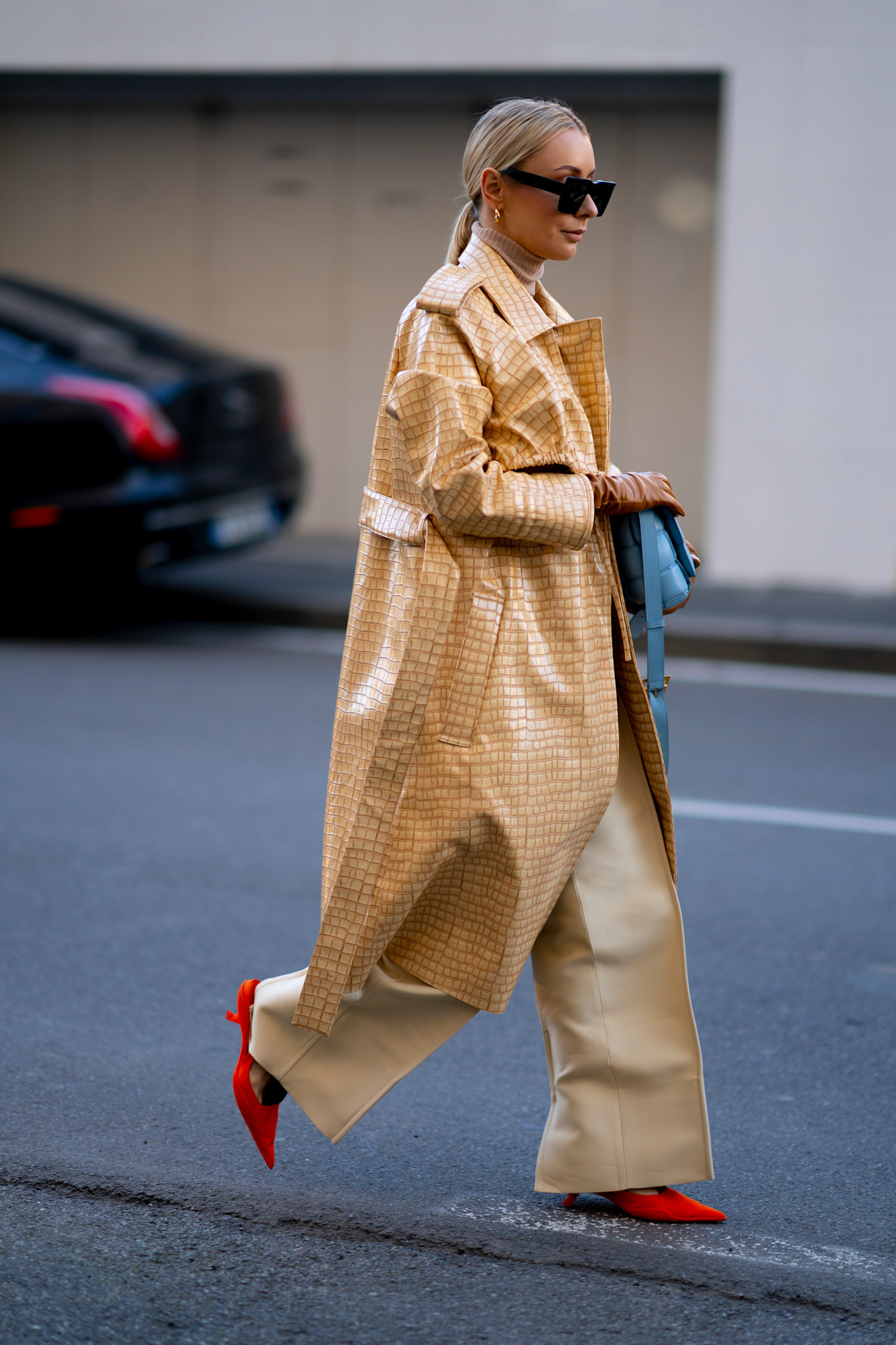 Trench-coat en cuir ouvré avec un pull à col roulé et un large pantalon de costume beige avec des escarpins en daim rouge.