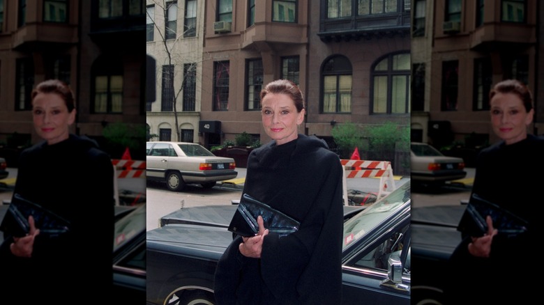Audrey Hepburn dans la rue de New York pendant la journée, vêtue d'un manteau noir.