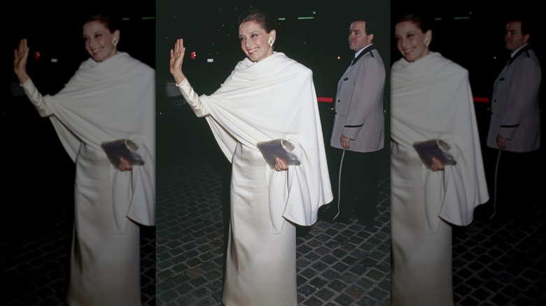 Audrey Hepburn aux Golden Globes, vêtue d'une robe blanche avec un châle blanc, saluant les caméras.