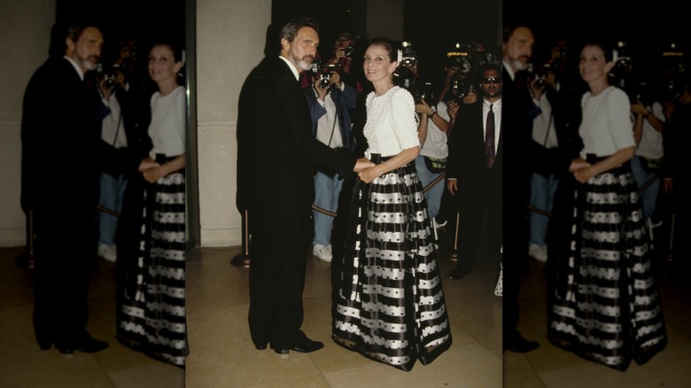 Audrey Hepburn lors d'un événement portant un haut blanc et une jupe ample à rayures noires et argentées.
