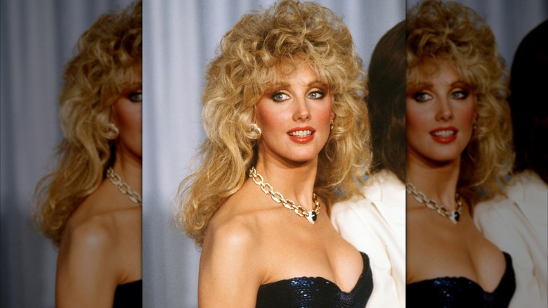Morgan Fairchild en 1982 lors d'un événement officiel, vêtue d'une robe scintillante et d'un collier en chaîne avec de volumineux cheveux bouclés.